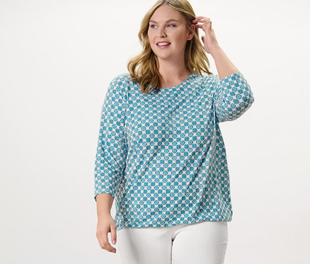 Nő pózol nyomott mintás női blúzban és fehér 7/8-os sztreccsnadrágban.