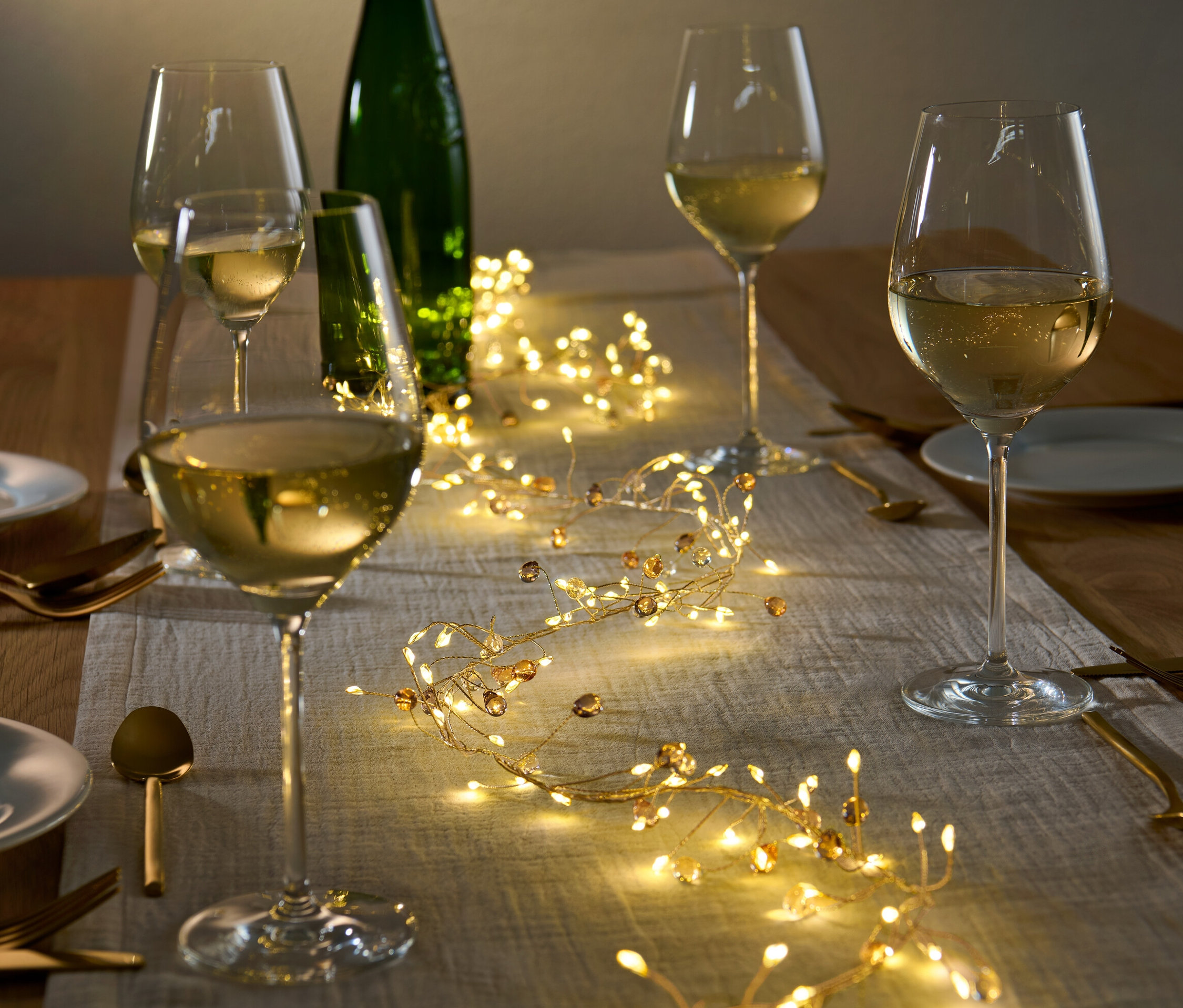 Megterített asztal LED-es girlanddal, borospoharakkal és tányérokkal.