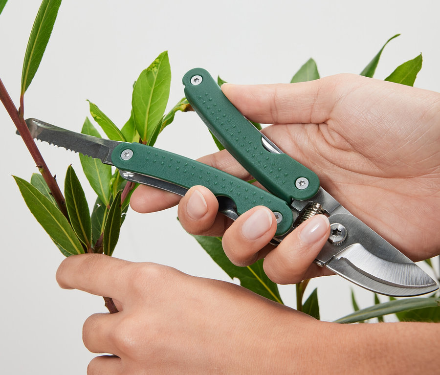 Egy személy egy ágat vág multifunkcionális kerti ollóval.