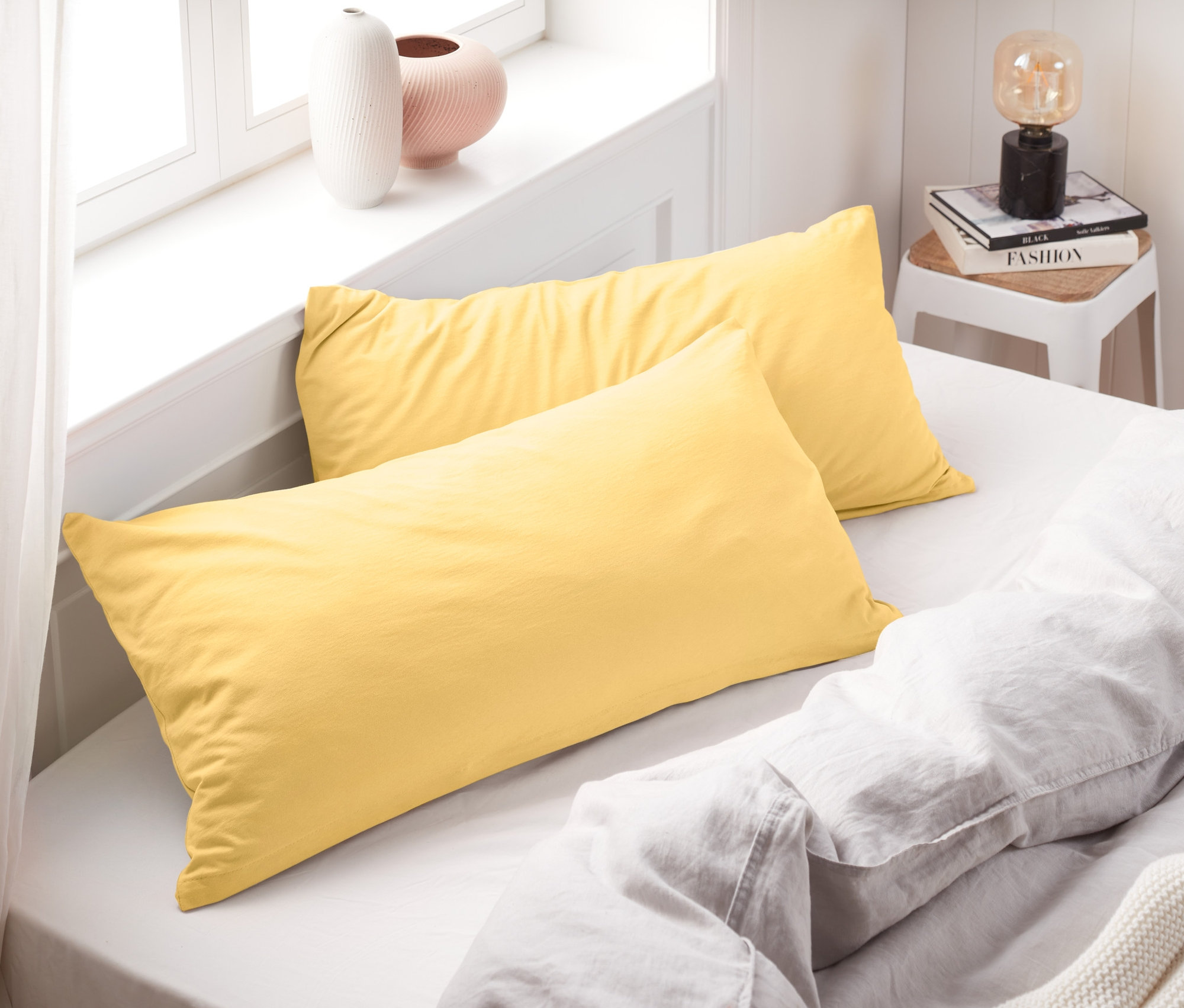 Két sárga dzsörzé párnahuzat fekszik egy ágyon fehér lepedőkkel.