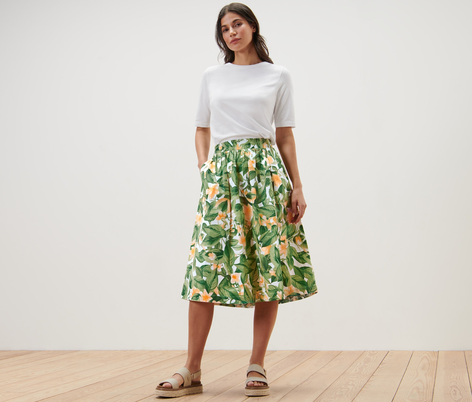 Nő pózol fehér pólóban és nyomott mintás poplin szoknyában.