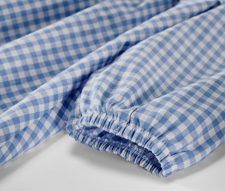 Kislány szövött ruha részlete kék-fehér kockás mintával és hosszú ujjakkal.