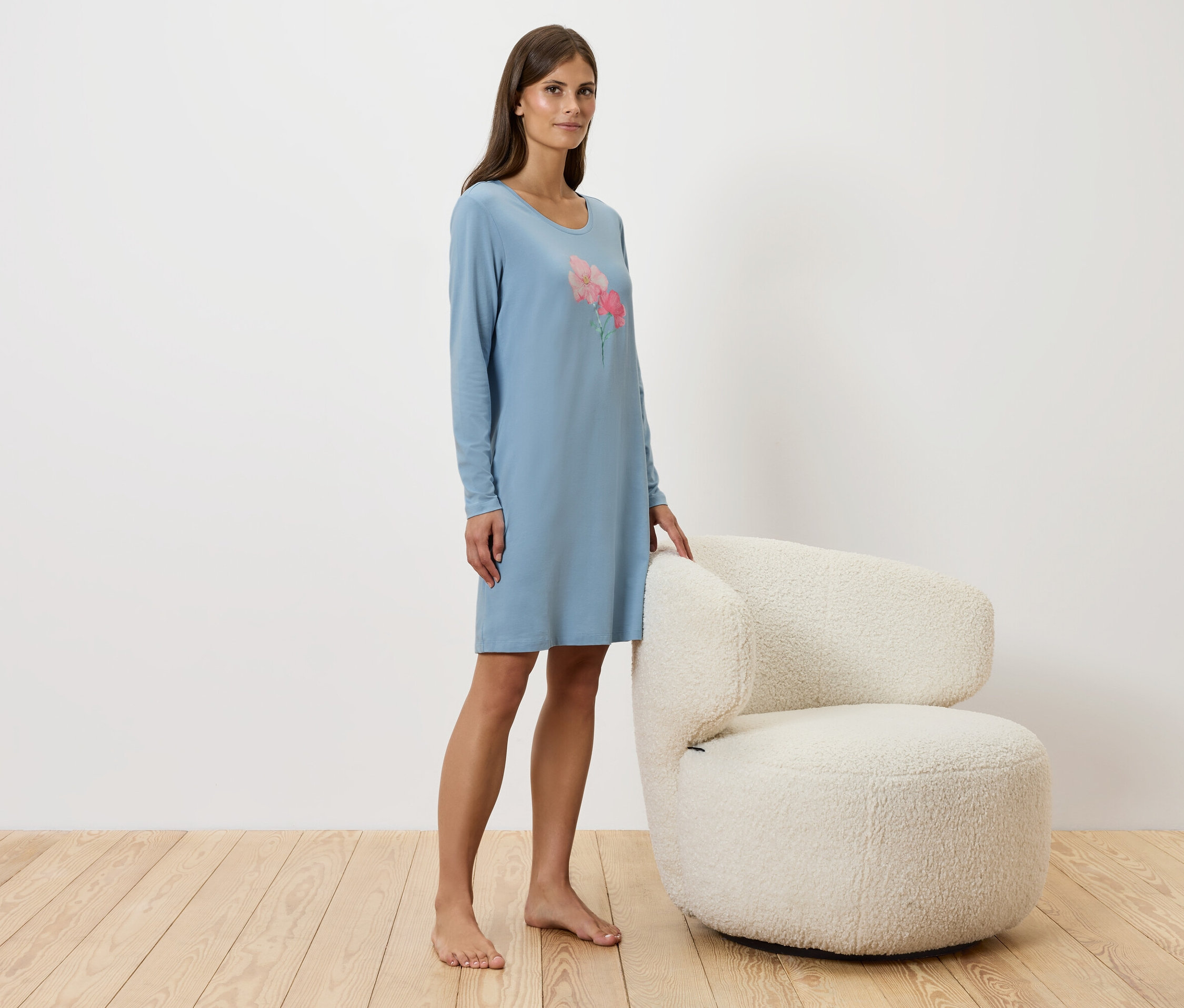 Egy nő áll egy fehér szék mellett, kék hálóinget visel.