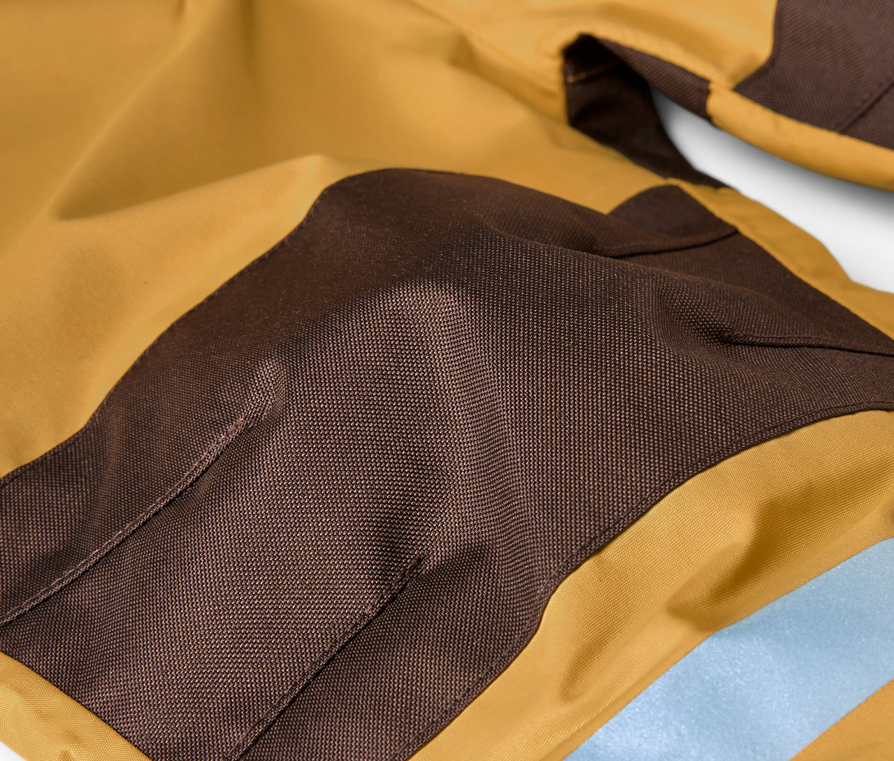 Egy barna és okker színű eső elleni kezeslábas részlete.