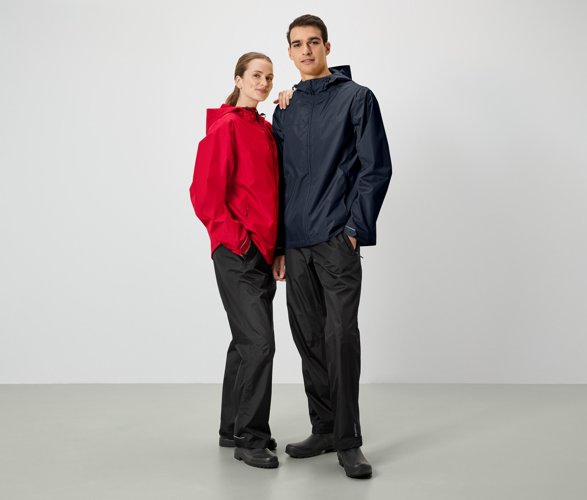 Egy férfi és egy nő egymás mellett pózol. Mindketten esőkabátot és fekete nadrágot viselnek.