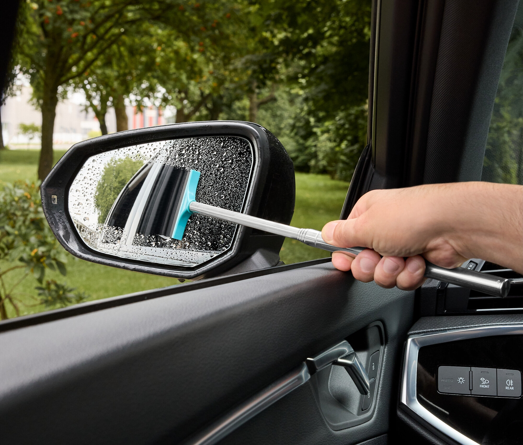 Férfi törli le a vizet egy autó oldalsó tükréről egy kék gumis ablaktörlővel.