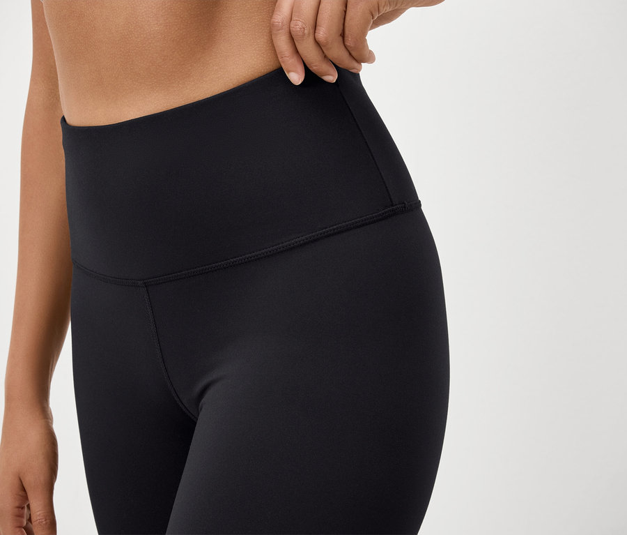Közeli kép egy fekete, magas derekú leggingset viselő nőről, aki igazítja a derékrészt.