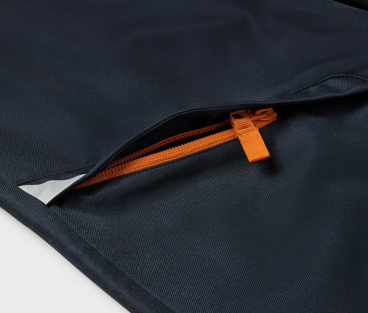 Egy gyerek softshell nadrág részlete, narancssárga cipzárral a zseben.