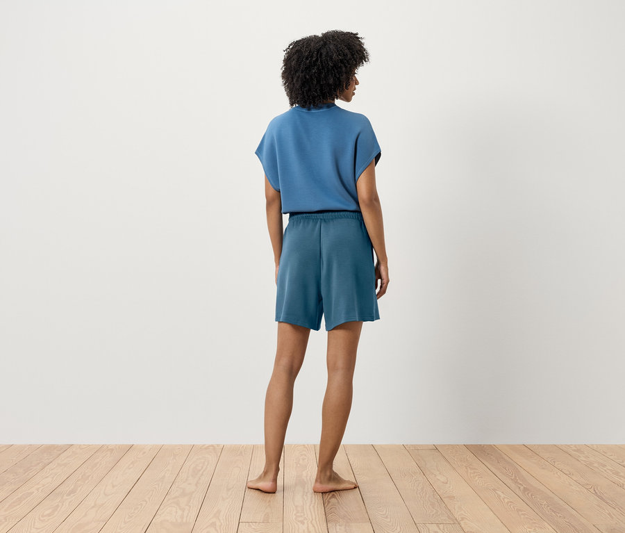 Nő kék pólóban és rövidnadrágban áll háttal a kamerának.