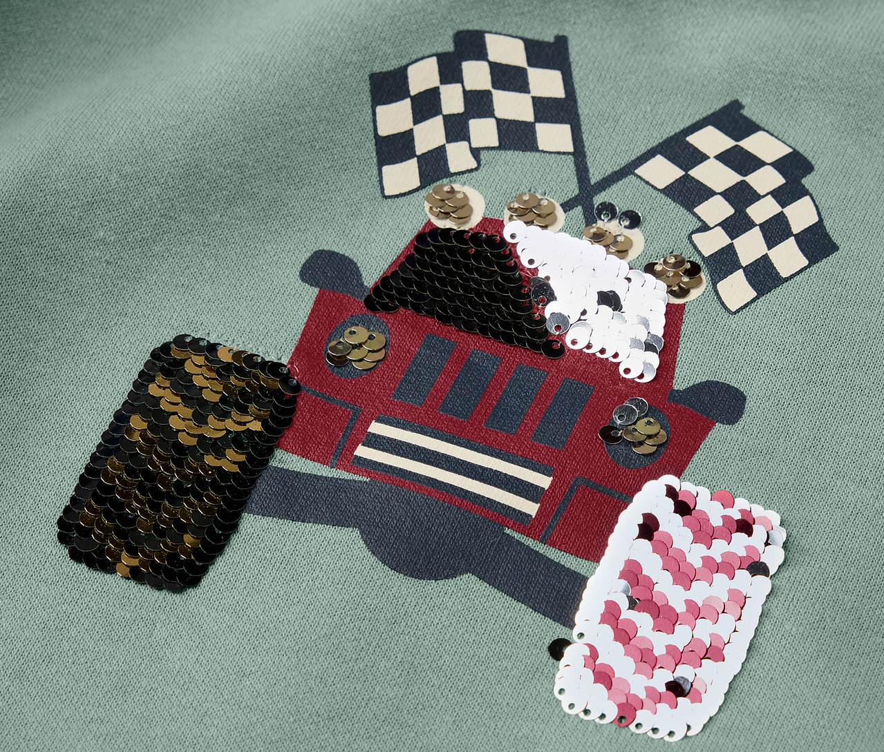 Egy Kinder-Sweatshirt részlete teherautó applikációval és kockás zászlókkal.