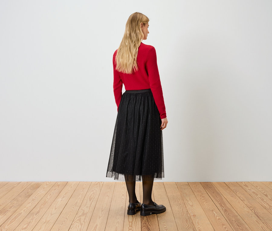 Egy nő háttal a kamerának piros pulóvert és fekete szoknyát visel.