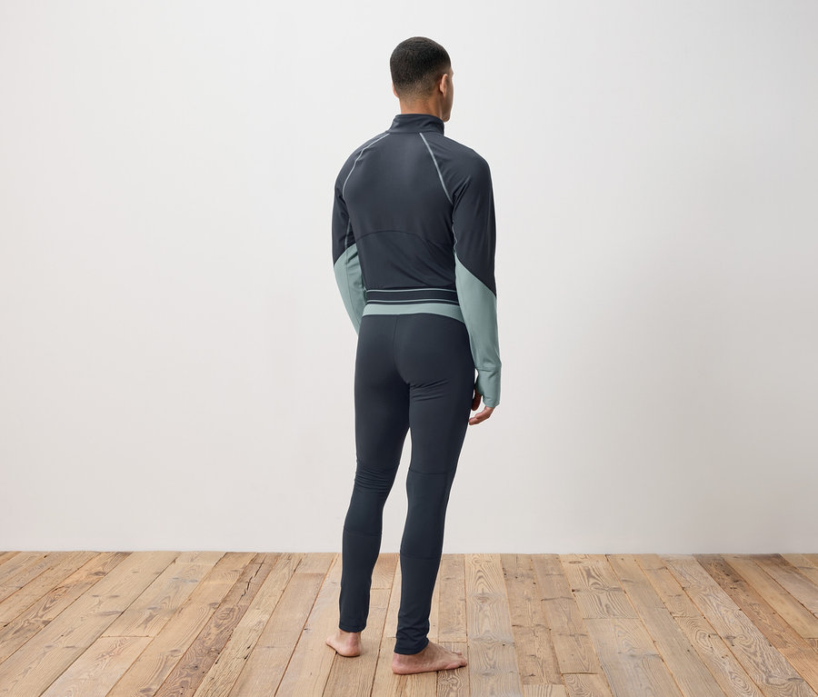 Egy férfi hátulról sötétszürke hőálló ruházatban, fapadlón állva.