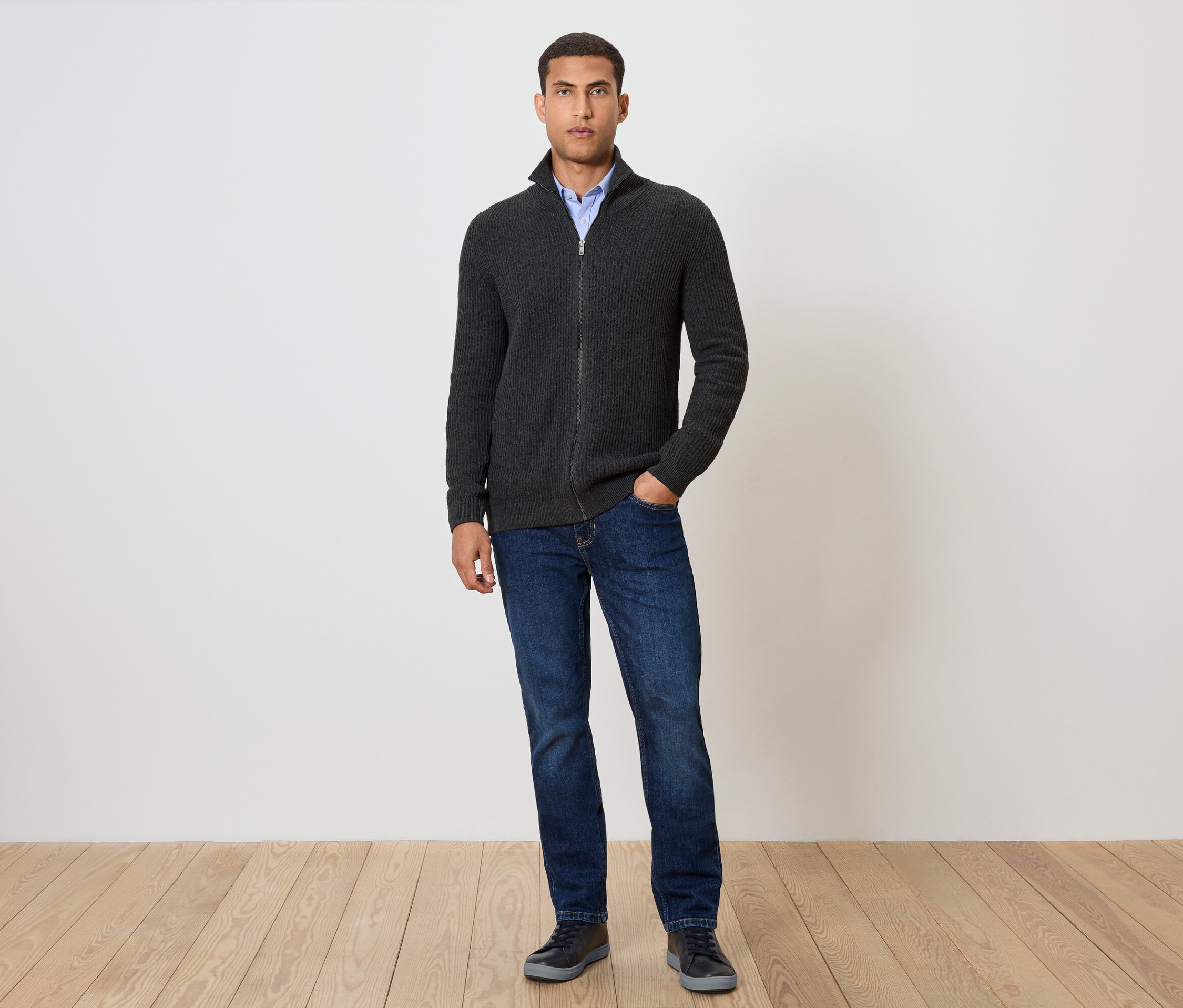 Férfi áll, és Kötött kardigánt, melírozott antracitot, farmert és cipőt visel.