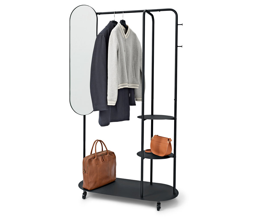 Fekete ruhatartó állvány ovális tükörrel, kabáttal, pulóverrel, nadrággal és két barna táskával.