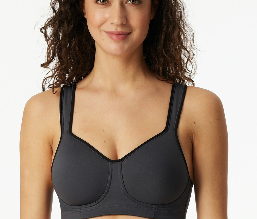 Egy mosolygó nő szürke sportmelltartót visel.