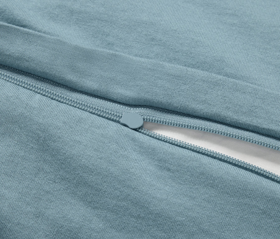 Egy világoskék cipzáros ágyneműhuzat részlete fehér anyagdarabbal.