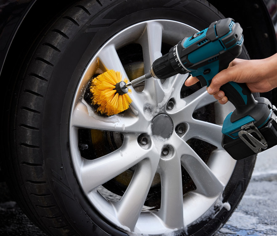Férfi tisztítja az autó kerekét egy fúrógéphez rögzített sárga kefével.