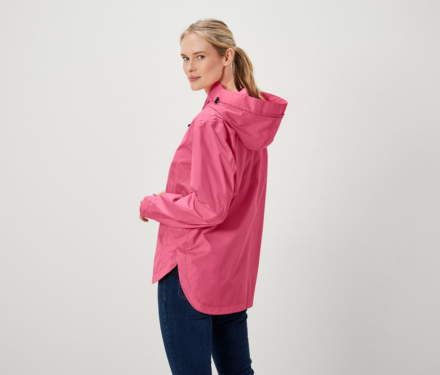 Egy nő a válla fölött néz, rózsaszín kabátot és farmert visel.