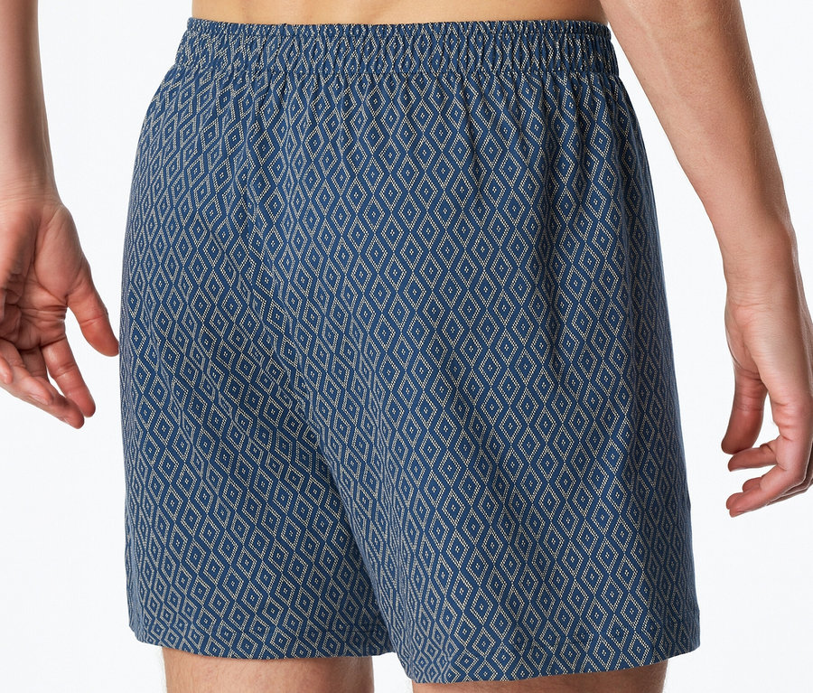 Egy férfi kék SCHIESSER jersey boxeralsót visel rombuszmintával és gumírozott derékkal.