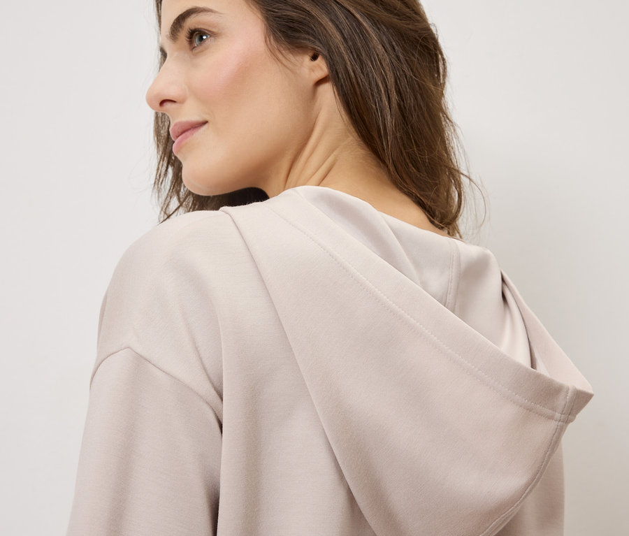 Nő visel egy világosbarna kapucnis pulóvert.