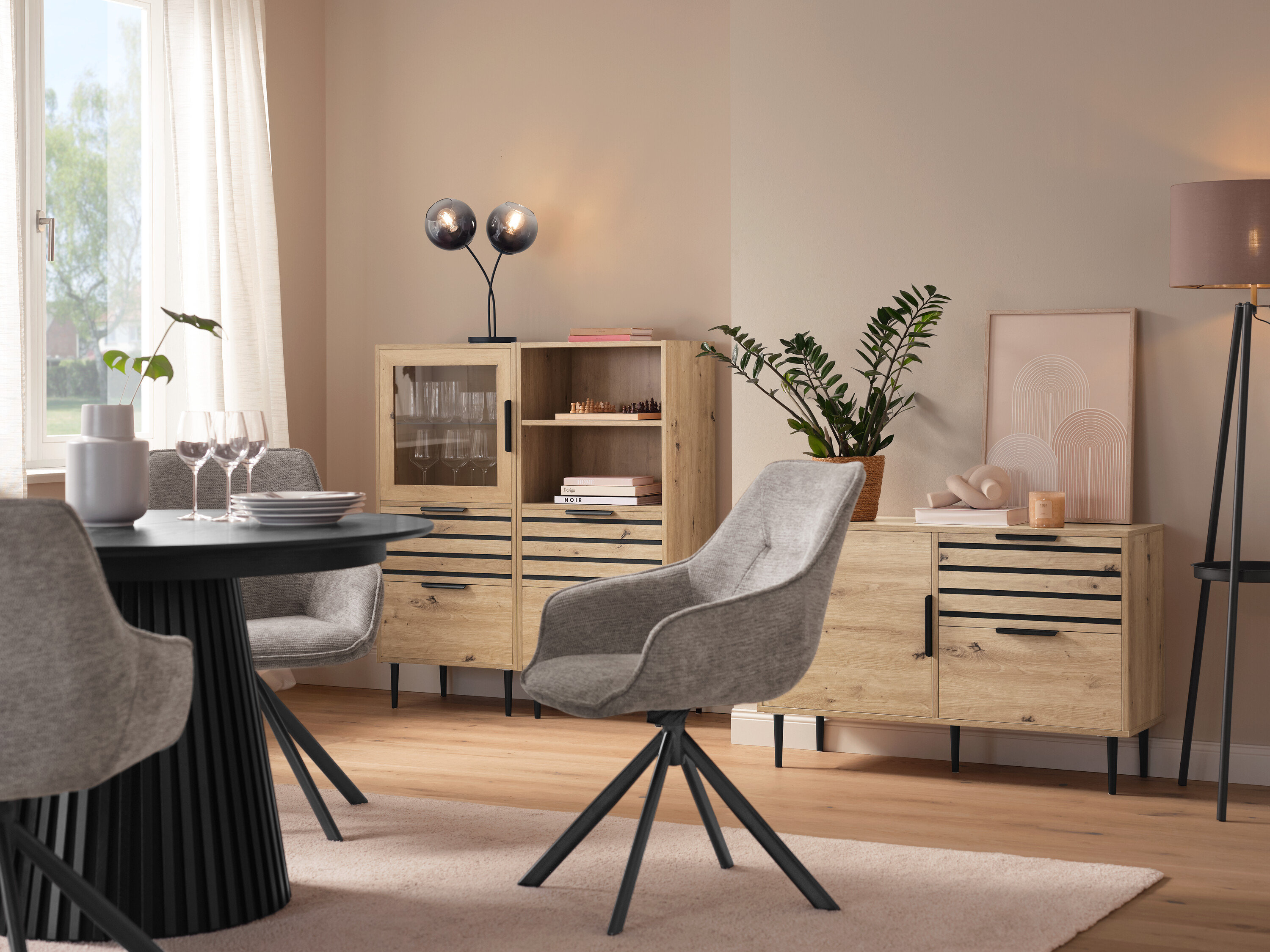 Étkező kerek asztallal, szürke székekkel, egy »BAAKEN« üvegajtós vitrinnel, egy »BAAKEN« fiókos polccal és egy fiókos szekrénnyel.