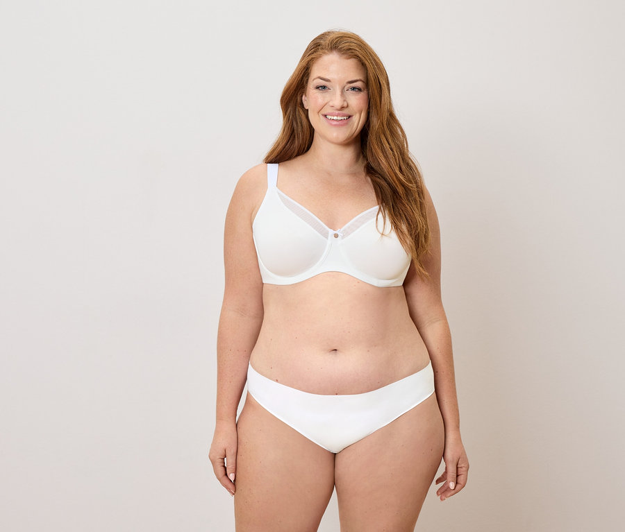 Hosszú vörös hajú, fehér melltartót és bugyit viselő, mosolygó nő.