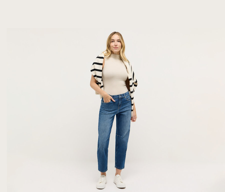 Nő Angels denim »Evi« farmerben, bézs felsőben és fekete-fehér csíkos kardigánban.