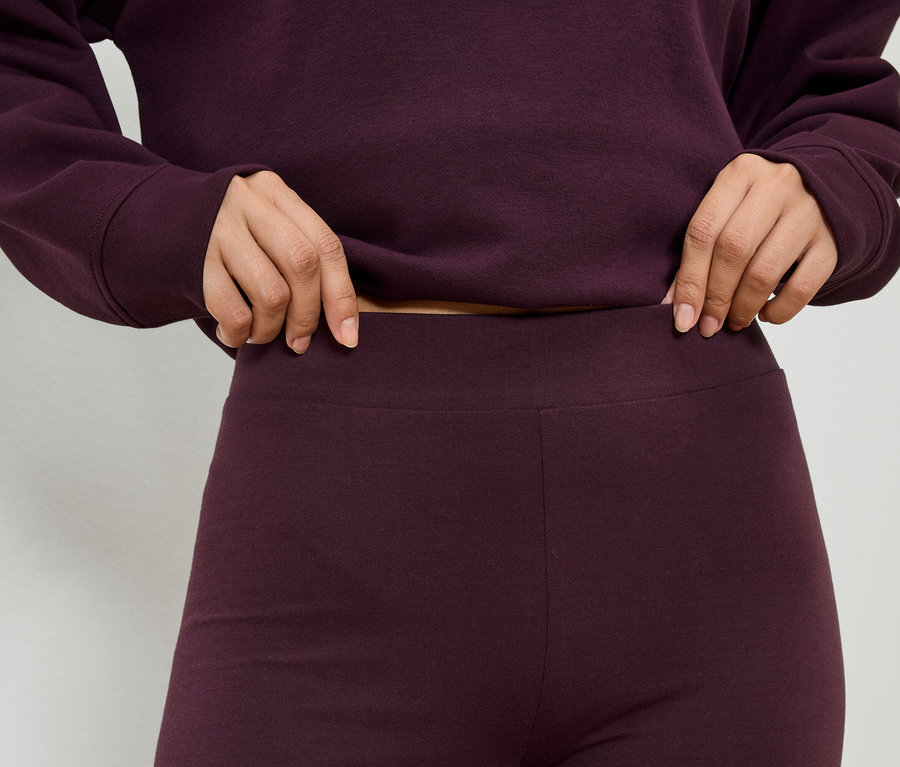 Egy bordó felsőt és leggingset viselő személy közeli képe, aki a leggings derekát fogja.