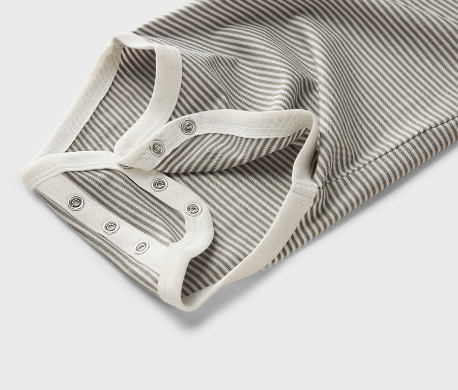 Közeli kép egy csíkos baba bodyról, patentokkal és fehér szegéllyel.