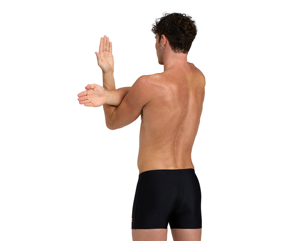 Férfi nyújtja a karjait, fekete úszónadrágot visel.