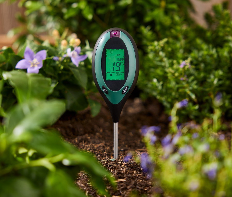 Egy zöld talajvizsgáló a növények közötti talajba van szúrva.