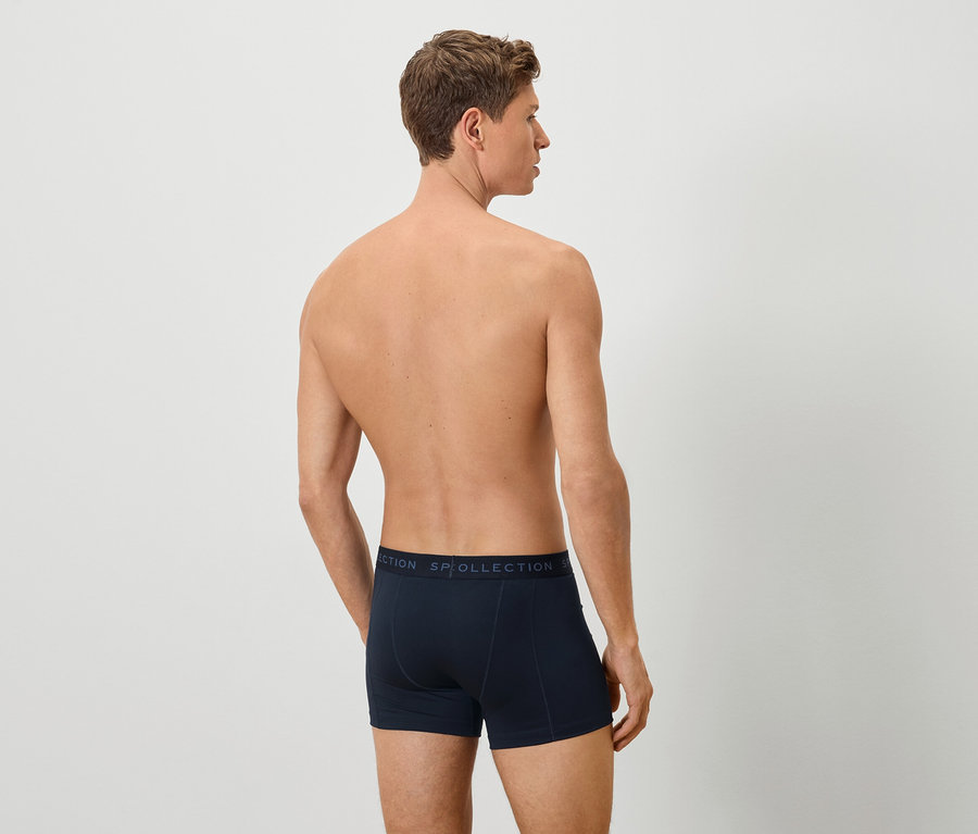 Hátulnézet egy férfiról, aki sötétkék boxeralsót visel, semleges háttér előtt.