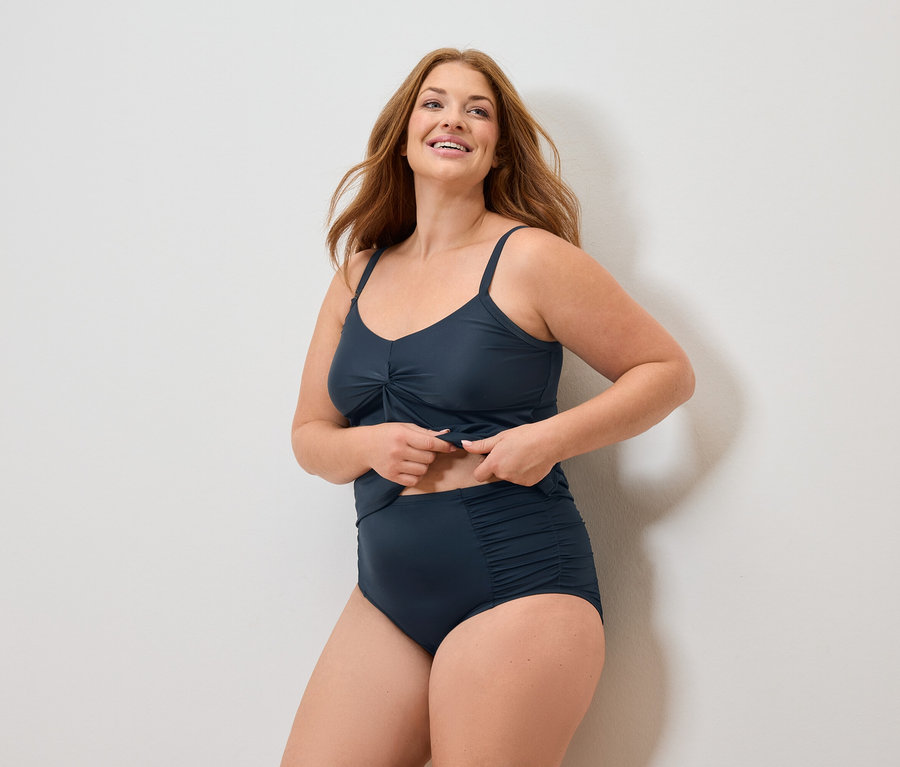 Hosszú vörös hajú nő sötétkék fürdőruhában mosolyog.