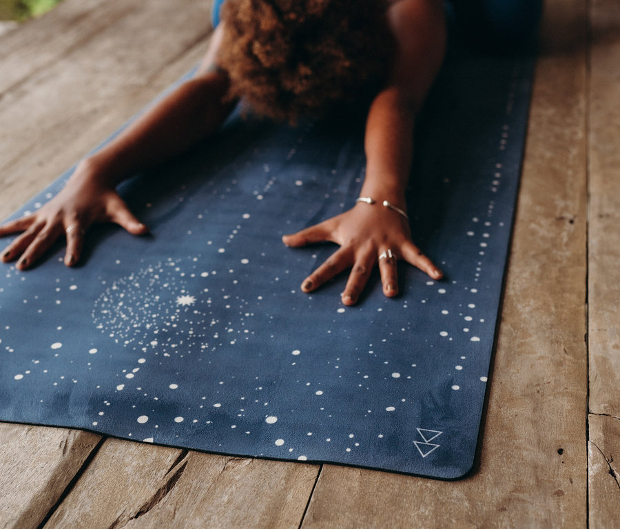 Nő nyújtózkodik egy kék, csillagos jógaszőnyegen, fa padlón.