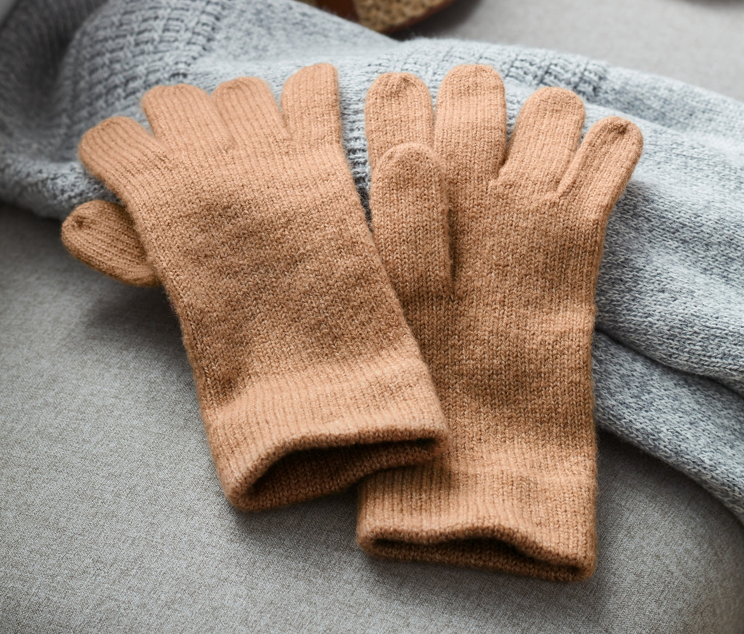 Bézs kötött kesztyűk egy szürke kötött takarón egy szalmatáska mellett.