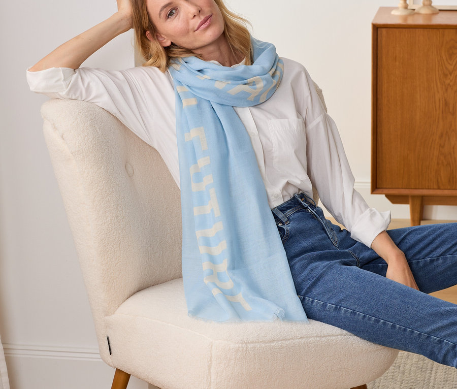 Nő ül a székben, világoskék színű, feliratos szövetsálat visel.