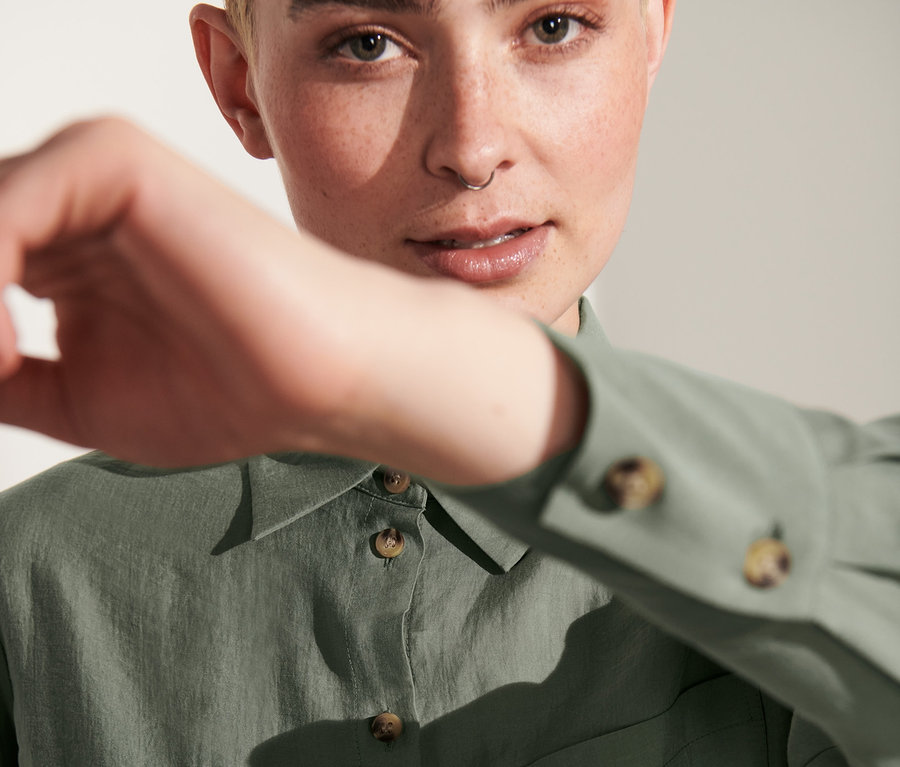 Nő takarja az arcát a kezével, és női ingblúzt visel.