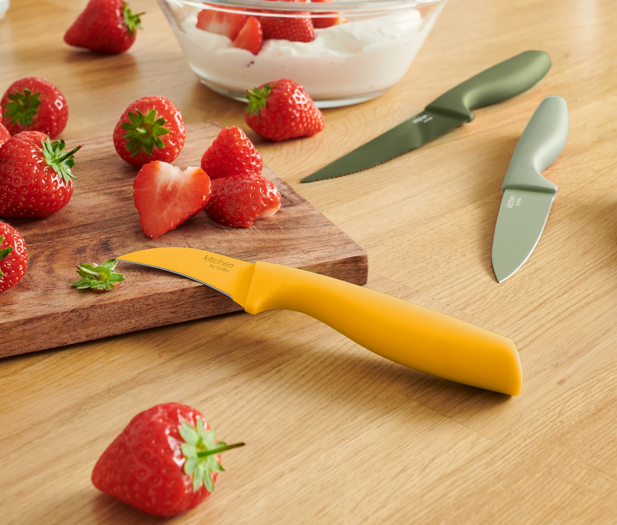 Egy fa asztalon eprek, egy tál eper és tejszín, valamint 3 konyhai kés található.