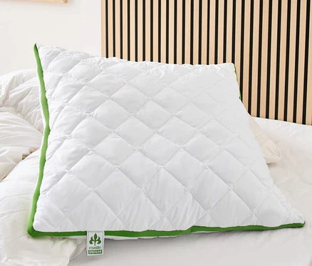 Egy fehér, steppelt irisette® greenline párna klímaszalaggal és zöld szegéllyel fekszik egy ágyon.