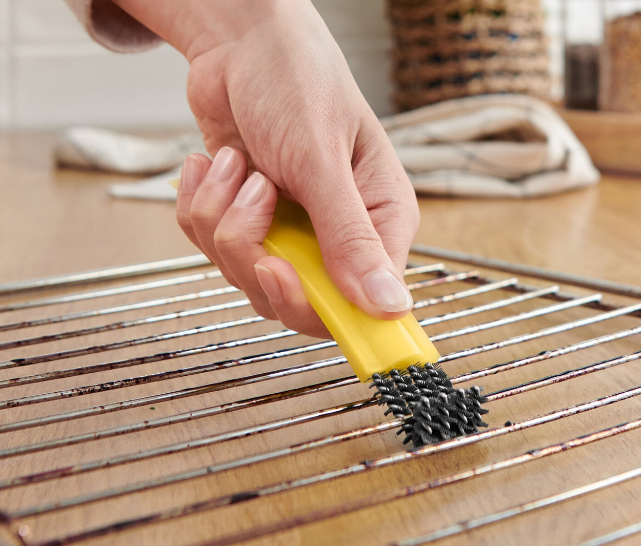 Nő tisztít egy sütőrácsot egy sütőtisztító kefével és kaparóval.