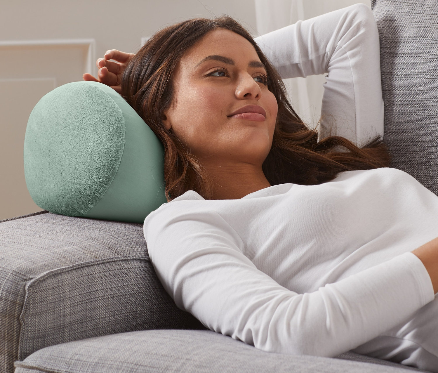 Nő fekszik egy szürke kanapén, a feje alatt egy relaxációs párnával.