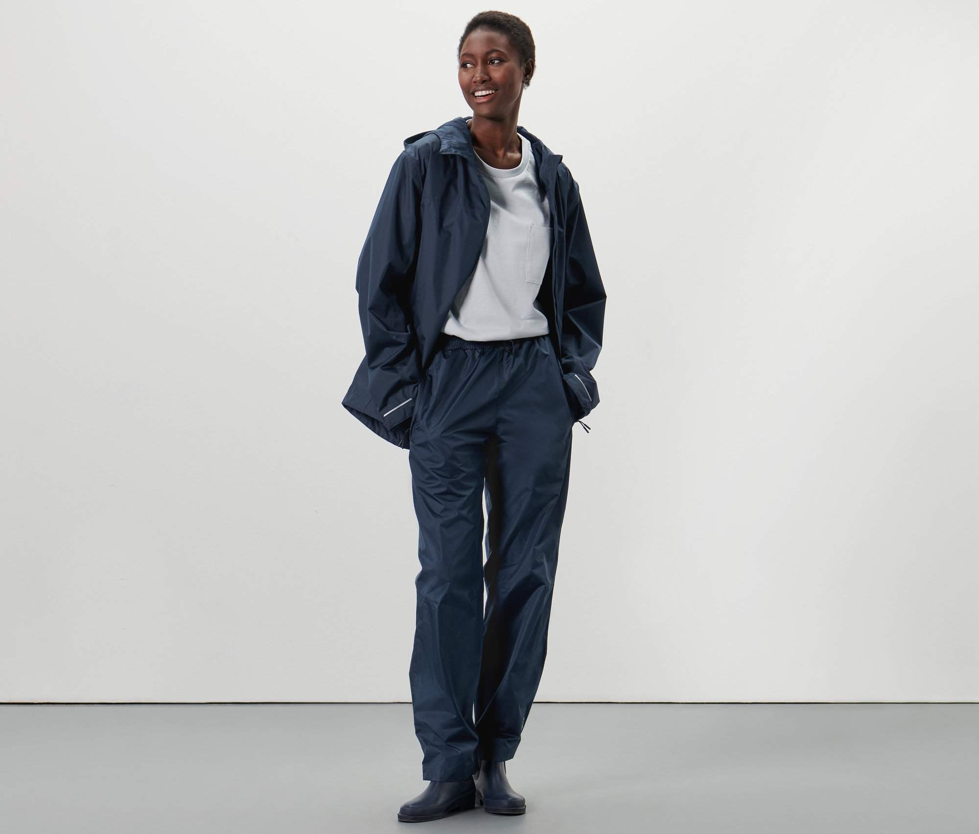 Egy afroamerikai nő áll, unisex esőnadrágot és esőkabátot visel.