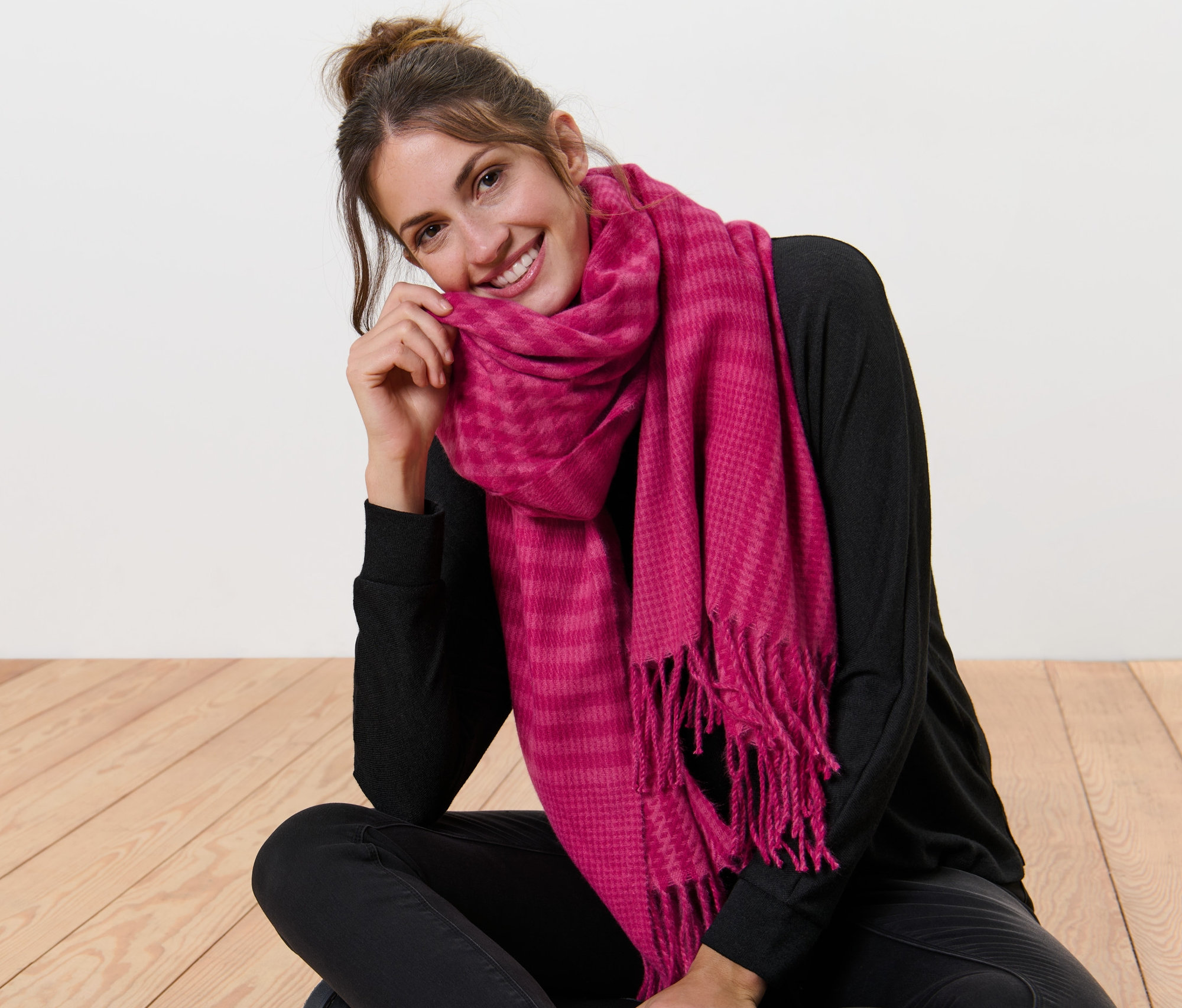 Egy nő ül keresztbe tett lábakkal a padlón, és egy málnapiros, tyúklábmintás szövetsálat visel.