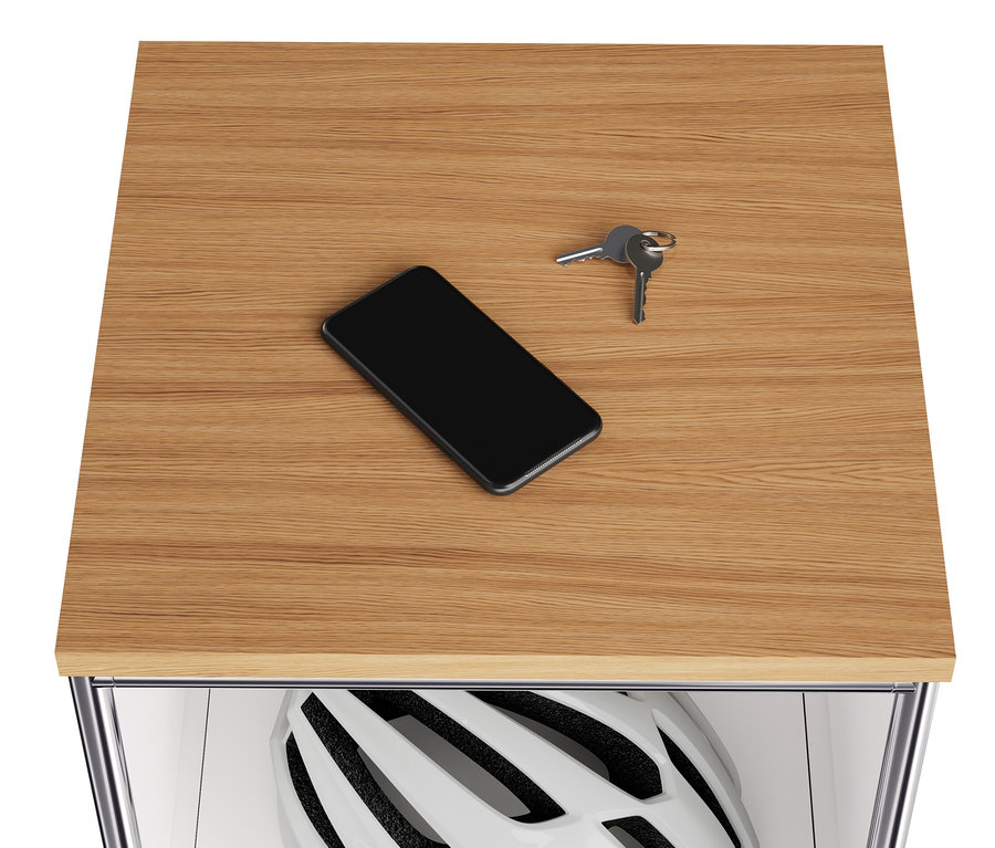 A keskeny, fehér »CN3« fém komód fa tetején egy mobiltelefon és kulcsok találhatók. A lenyíló rekeszben egy sisak van.