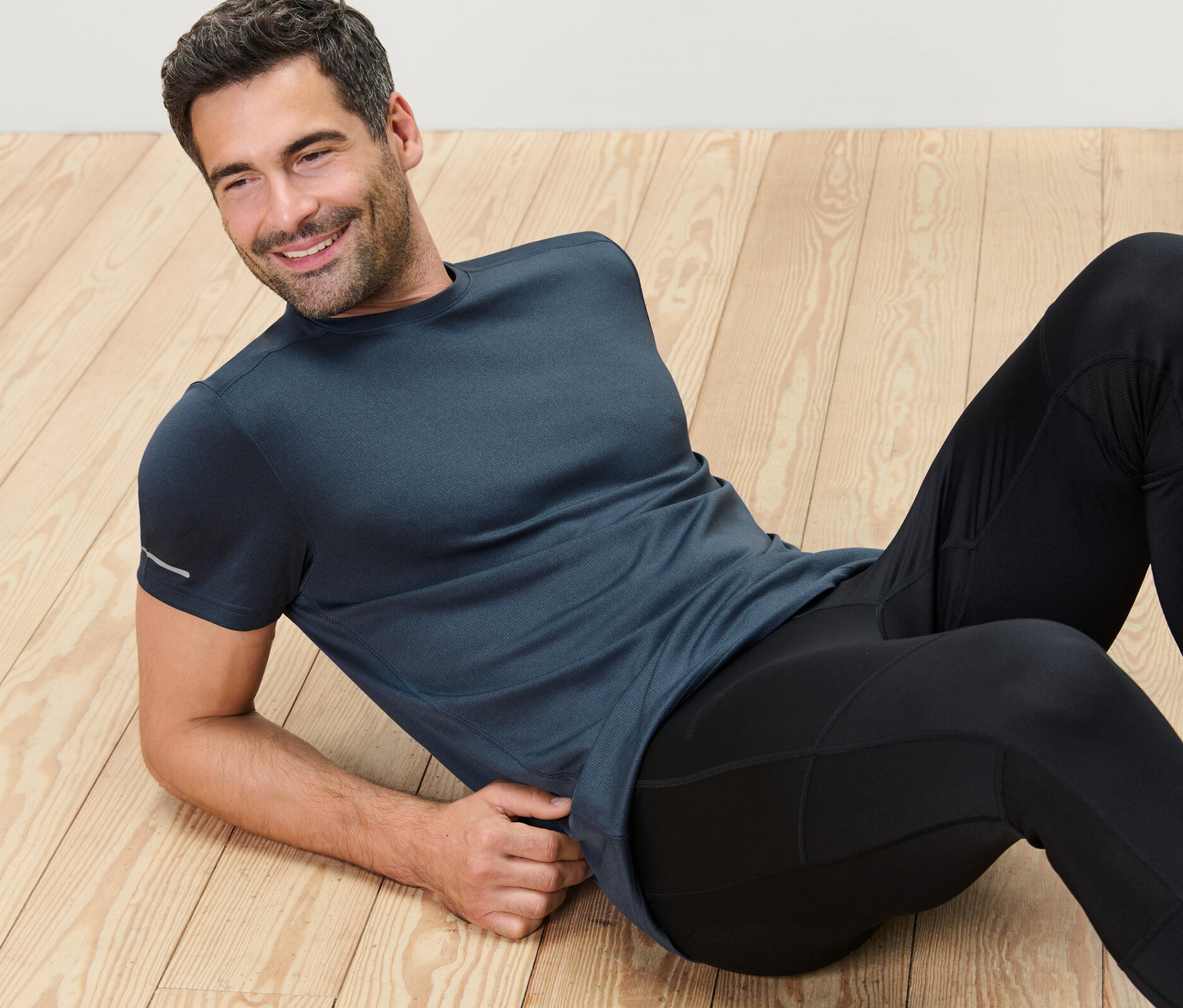 Férfi fekszik a fapadlón, kék színű funkcionális felsőt visel.