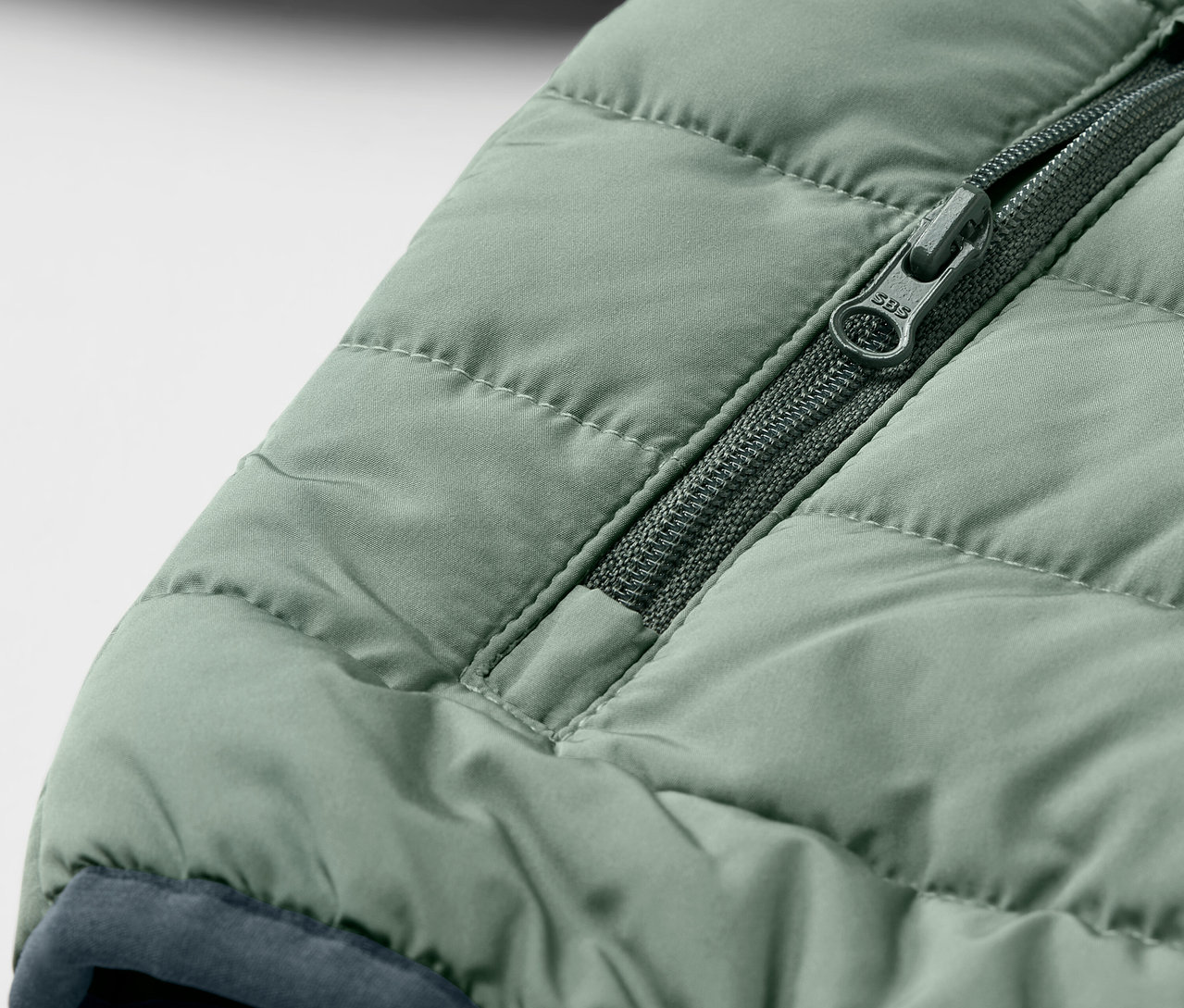 Egy zöld, steppelt gyerekkabát részlete cipzárral.