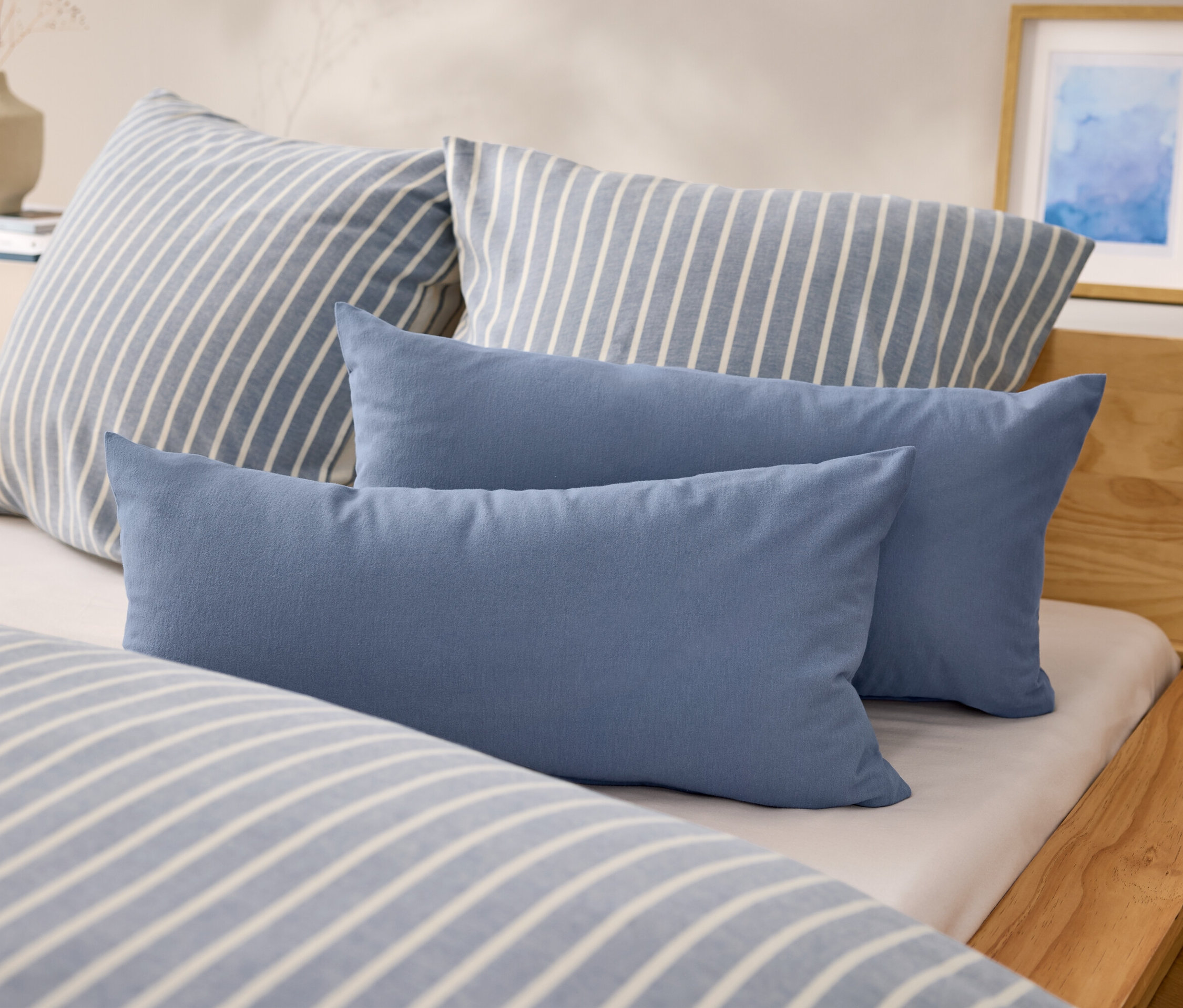 Az ágyon két kék, téglalap alakú párna és két kék-fehér csíkos párna található.