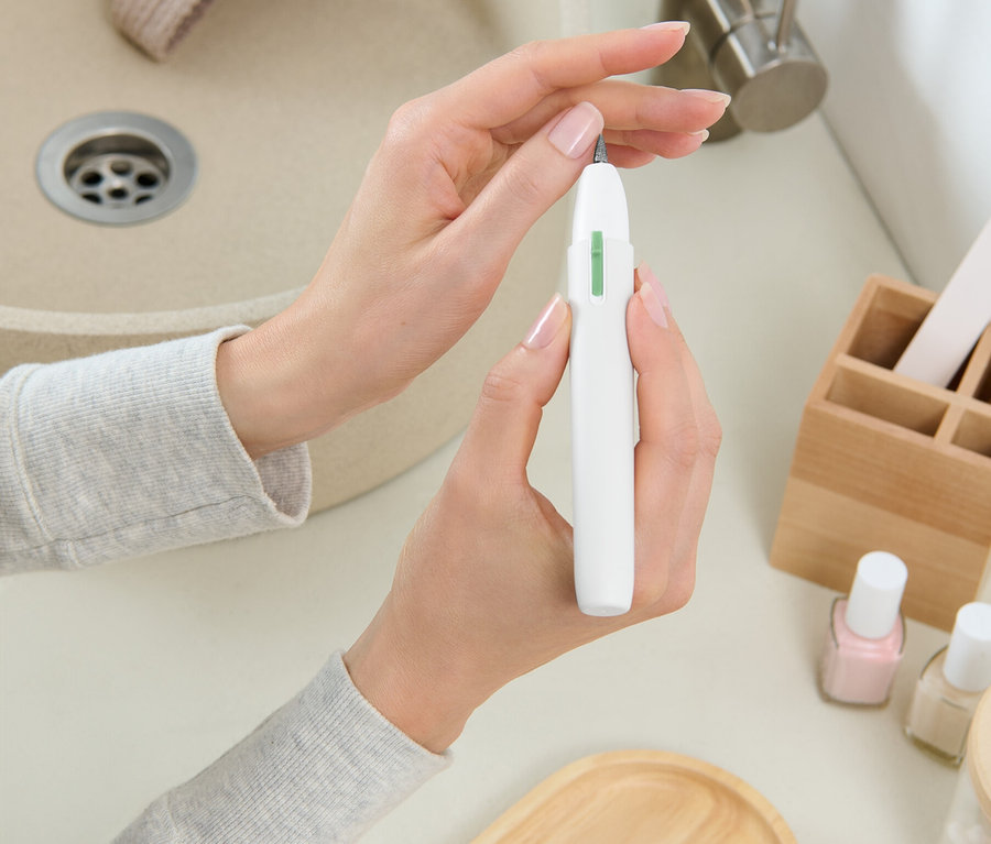 Egy nő fehér körömmarót tart a mosdó előtt.