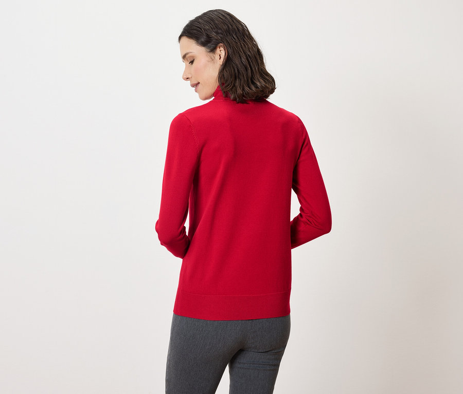 Hátulról látható egy sötét hajú nő, aki piros pulóvert és szürke nadrágot visel.