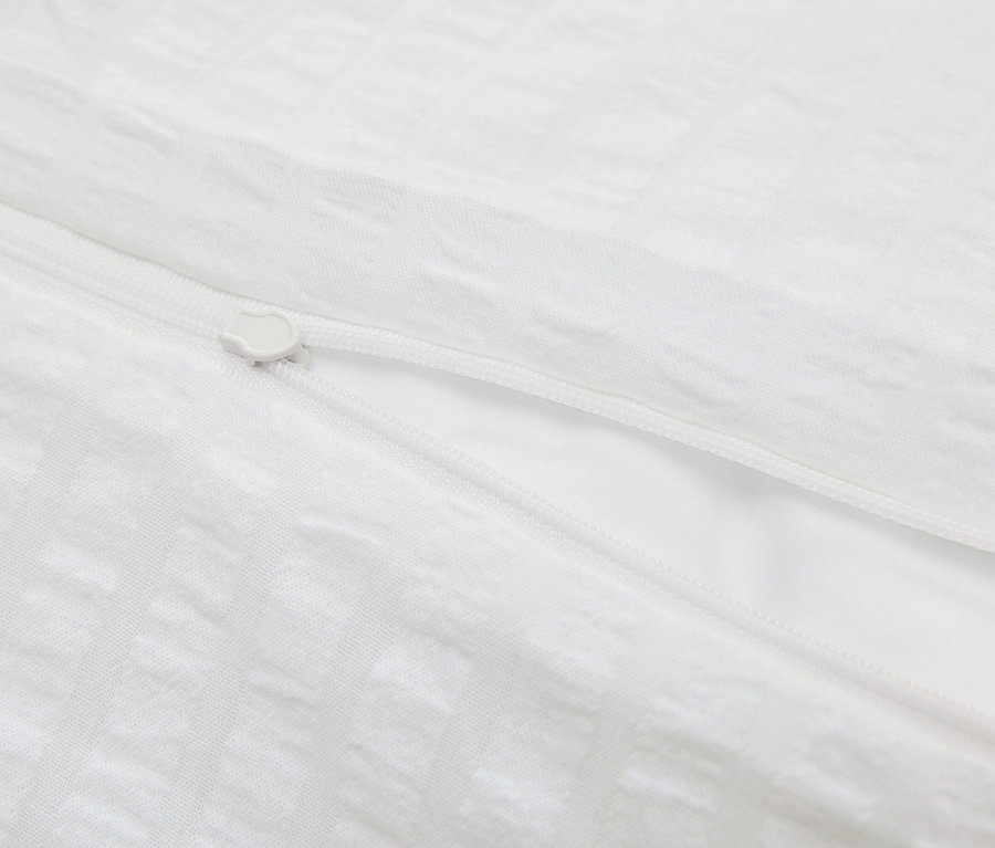 Egy fehér, cipzáras ágyneműhuzat részlete.